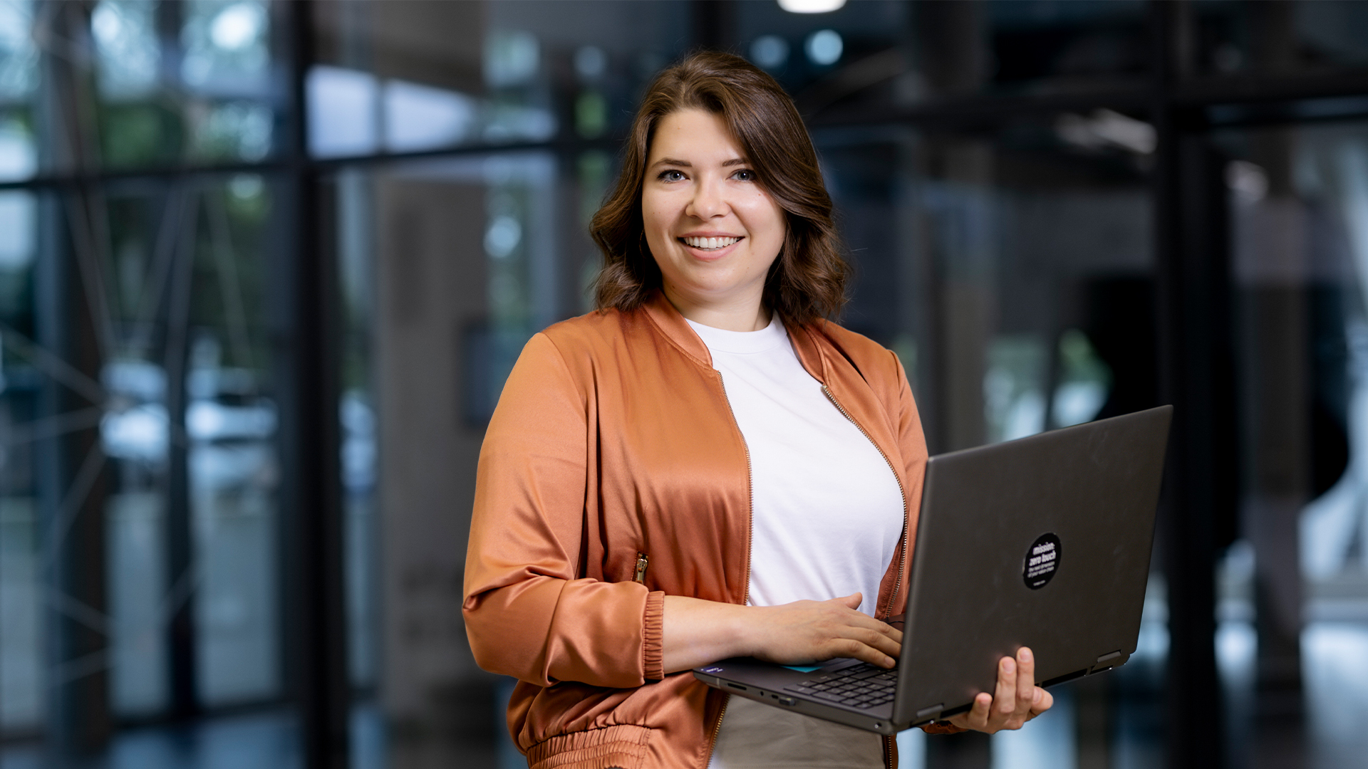 Anita hält einen Laptop und lächelt freundlich in die Kamera