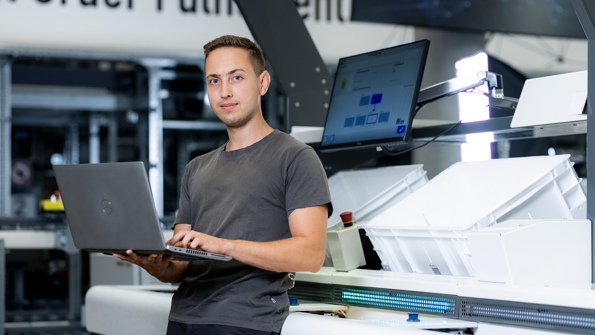 Ein Software-Inbetriebnehmer steht mit einem Laptop vor einer Arbeitsstation im Lager