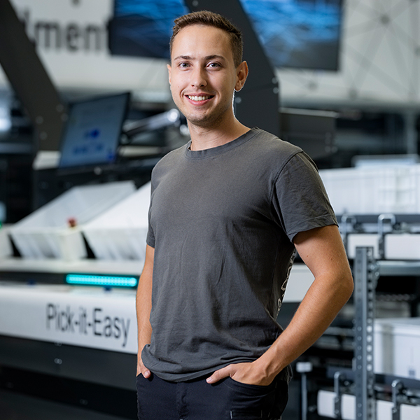 Software commissioning engineer Sebastian stands, smiling, in a warehouse.